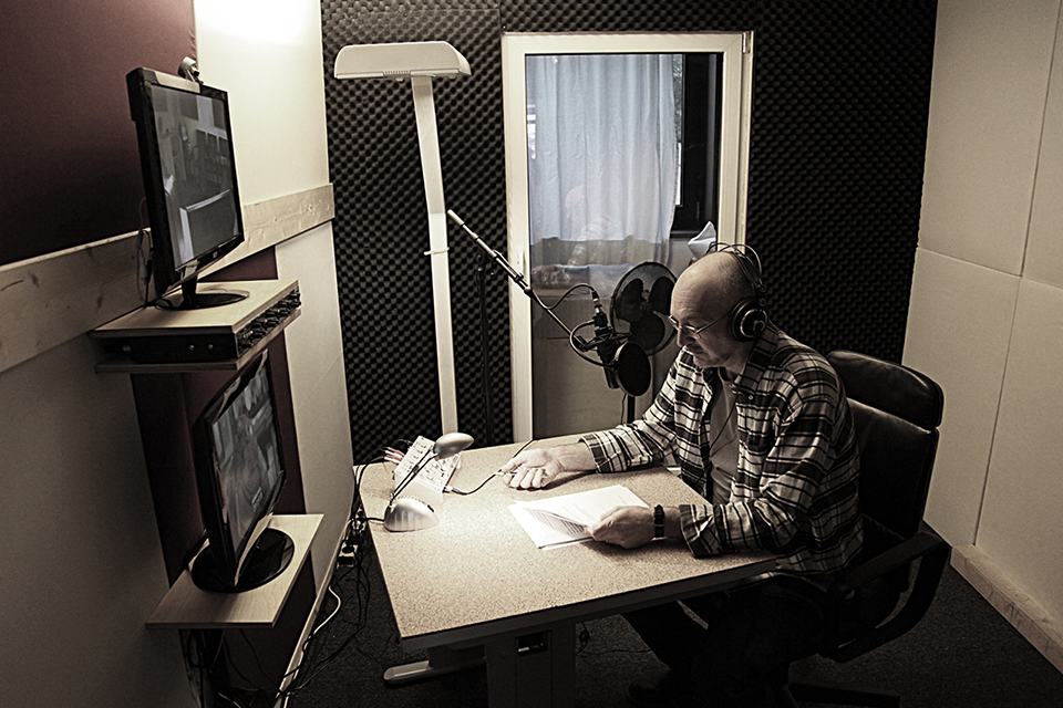 Ein Sprecher sitzt im Tonstudio und liest aus seinem Skript